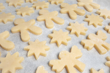 Many cookies on baking sheet. Diagonal rows of short bread cookies dough in different shapes such as: star, gingerbread man and angel. Traditional Christmas baking, home made dough. Selective focus.