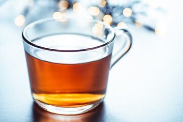 Glass cup of hot aromatic tea on white background with spices. Christmas tea with oranges on bokeh lights background. Christmas tea.
