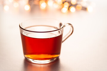 Glass cup of hot aromatic tea on white background with spices. Christmas tea with oranges on bokeh lights background. Christmas tea.
