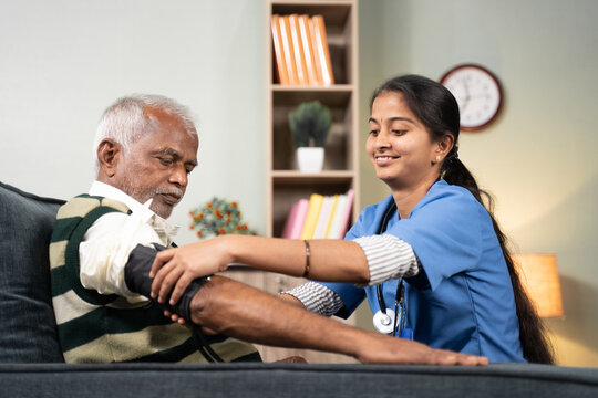 Nurse of doctor busy in setting up BP or blood pressure medical equipment to senior man at home of check up at home - concept of routine home help check.