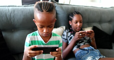 African siblings using cellphone at home. Black ethnicity children watching video on cellphone - Powered by Adobe