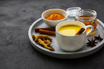 Yellow turmeric latte drink. Golden milk with cinnamon, turmeric, ginger  and honey over black concrete background.