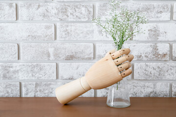 Wooden hand holding vase with flowers on table