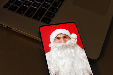 Naklejka premium Santa Claus calls on a smartphone and makes a video greeting with New Year and Merry Christmas.