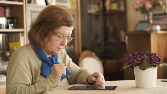 Tablet. Senior adult using digital technology device indoors. Touching screen.