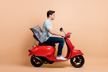 Profile side view portrait of nice cheerful guy driving red moped spending spring weekend isolated over beige pastel color background
