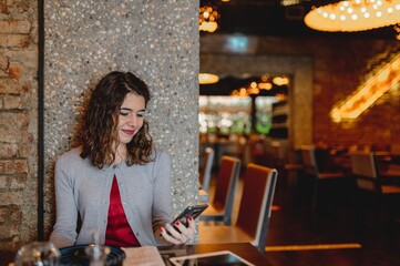 Copy space in close-up smiling woman portrait. Attractive young caucasian lady sitting in a table restaurant using smartphone. Electronic devices, technology, communication concept.