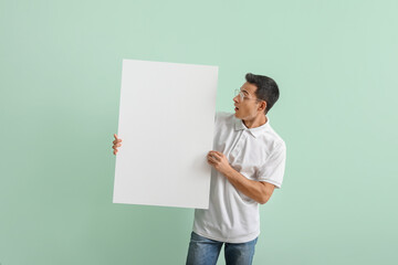 Surprised young man with blank poster on color background