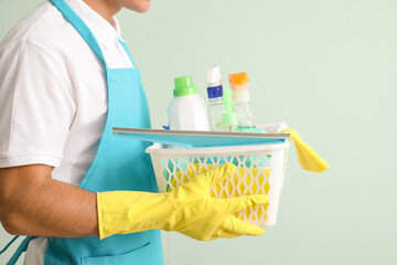 Young man with cleaning supplies on color background
