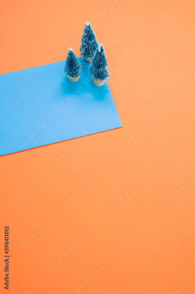 Wall mural Vertical shot of Christmas pine figurines on blue and orange background for a copy space