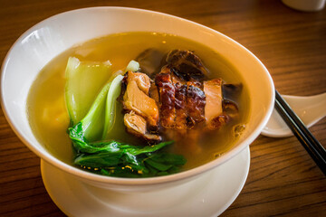 a bowl of chinese wanton noodle soup with chicken char siew and vegeatable on top