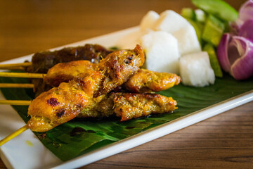 a plate of chicken and beef satay with raw onions, cucumber, rice cake and peanut sauce on the side
