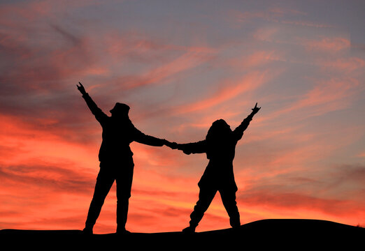 silhouette of girls holding hands on the mountain,  success people at summit. motivational and inspirational concept. hooding hands against sunset sky.