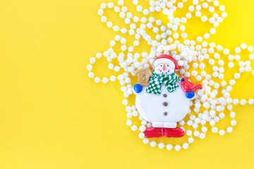 Snowman with Christmas beads on yellow background. Christmas background. New Year concept.