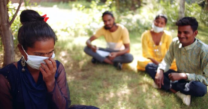 Slow-motion static medium-shot MS of one female in the nature park garden as she talks to her friends while she is maintaining social and physical distance while they all have pulled down their face m