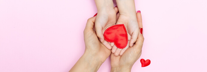 red heart in child and mother hands on pink background. concept of love, charity