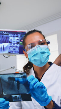 Patient pov in dental office planning surgery steps of teeth cavity, dentist pointing on x-ray image. Stomatology doctor wearing protective mask and gloves, working in modern stomatological clinic
