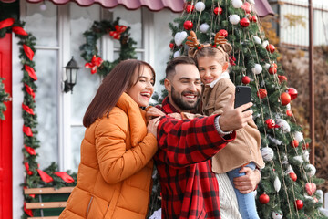 Fototapeta na wymiar Happy family taking selfie near house decorated for Christmas