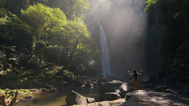 Beautiful woman travel in tropical rain forest jungle and enjoy amazing waterfall in the rays of the rising sun against the backdrop of scenery nature. 4K