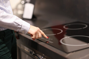 Female finger presses button on touch electric stove - obrazy, fototapety, plakaty