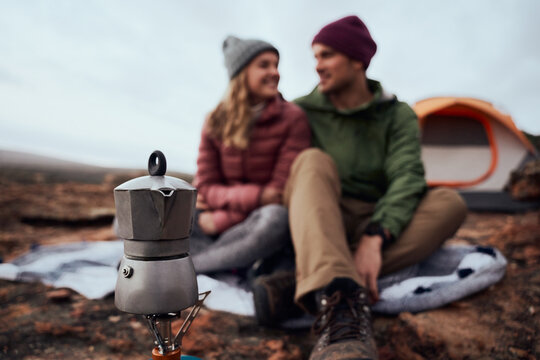 Closeup of kettle on gas stove during camping with smiling couple looking at each other during winter - young adventurous couple camping and making coffee