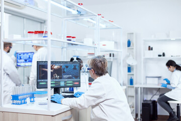 Elderly aged medical chemist working on powerful computer in modern facility. Senior scientist in...