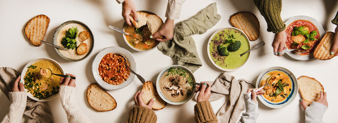 People eating Autumn and Winter creamy vegan soups, fall and winter vegetarian food menu. Flat-lay of peoples hands eating homemade soup with fresh bread over white table background, top view - 398416234