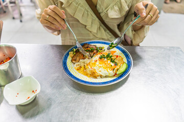 Vietnamese girl eating Com tam - a Vietnamese broken rice with pickles steak grilled pork ribs cucumber onion oil sweet chilies garlic fish sauce fried egg omelet Asian cuisine