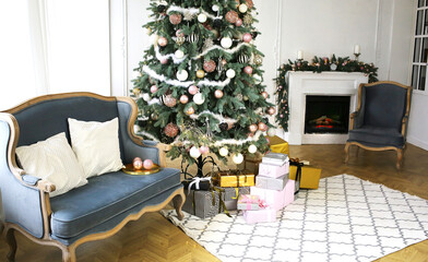 New Year's interior with сhristmas-tree by the fireplace, balls and lights. Comfortable blue sofa with pillows in the room. Classics in the interior. Modern design.