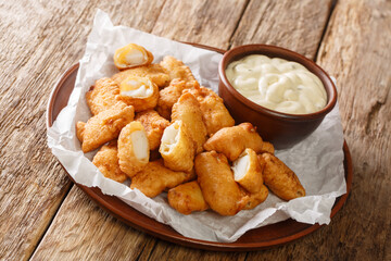 Popular Dutch street food Kibbeling item consisting of pieces of cod fish that are dipped in batter, deep-fried  and served with a dipping sauce closeup in the plate on the table. Horizontal