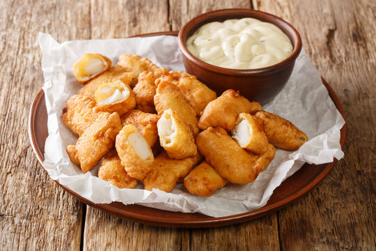 Fish appetizer consisting of deep-fried cod pieces and served with a dipping sauce closeup in the plate on the table. Horizontal