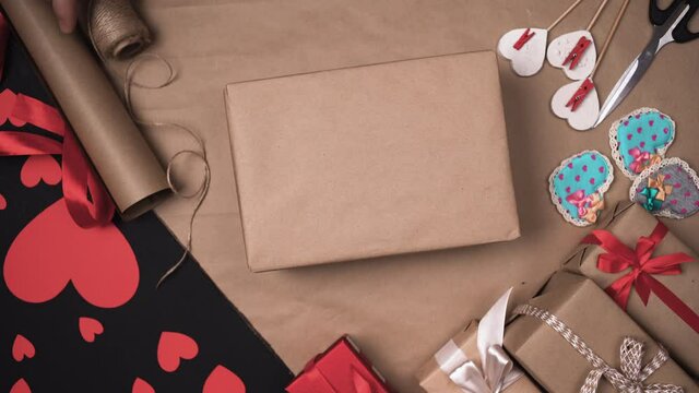 male hands put a box in craft paper on the table and start tying it with a string. The process of preparing gifts for the holiday. Valentine celebration concept