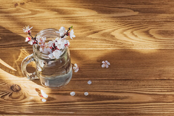 Glass jar with blooming spring branches on wooden table