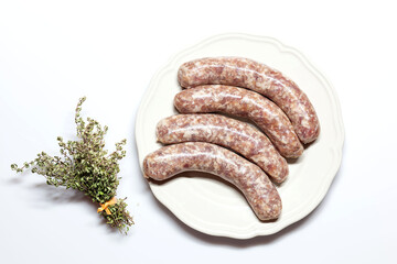 German raw bratwurst Pork Sausages on white with a bunch of thyme and multicolored pepper - seasoning, on a plate