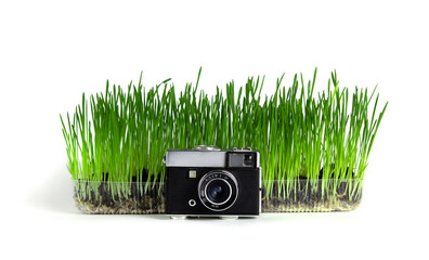 retro camera with small lens stands in front of a container with grass on a white background.