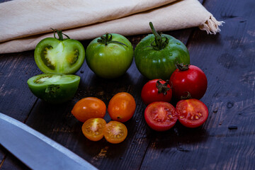 High angle shot of sliced ripe and unripe tomatoes with knife and napkin on a wooden table