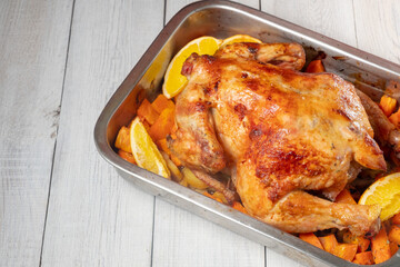 Whole baked chicken with carrots and oranges on a white wooden background. Close-up