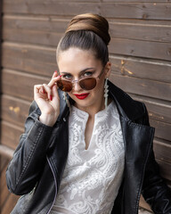 Beautiful bride woman in wedding dress and leather jacket. Fashion runaway. Fateful bride with a fashionable hairstyle and red lipstick on a wooden background