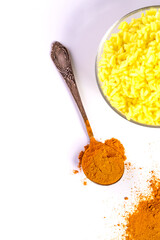 On the white table is a bowl of rice and turmeric in a spoon and on the table.