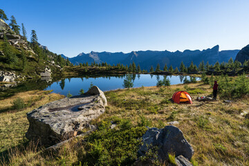 Hiker beside her red tent in the mountains of Ticino on a summers mornig.