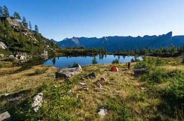 Hiker beside her red tent in the mountains of Ticino on a summers mornig.