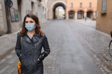 Fototapeta premium Copy space close-up portrait caucasian young woman walking in a city center during cold winter season. Lady wearing a protective face mask. Pandemic, new normal concept.