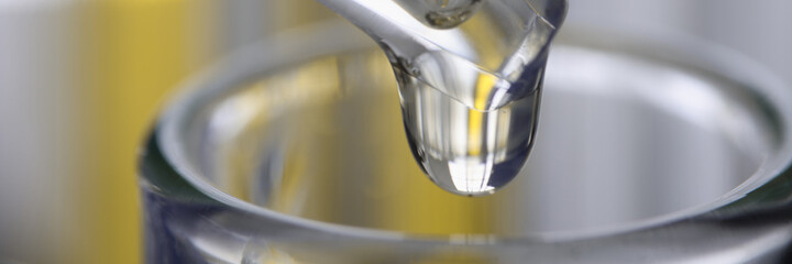 Chemical pipette dispenser drips yellow liquid into glassware closeup. Pharmaceutical industry concept.
