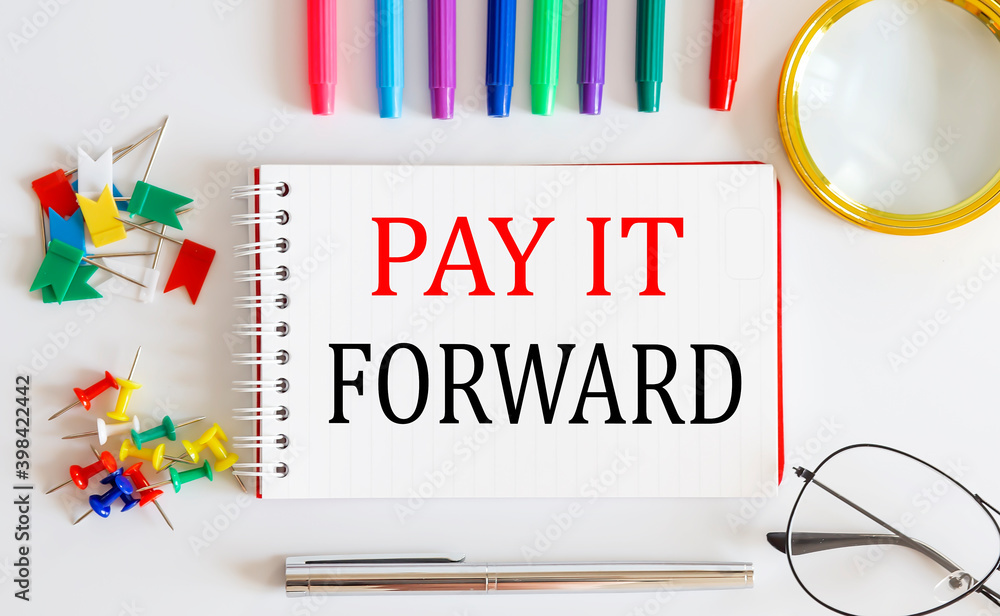 Poster notebook with pay it forward word with office tools on the white table.