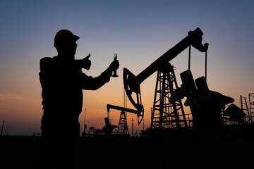 Silhouette of a chemical engineer taking a sample of crude oil against the background of oil pumps.