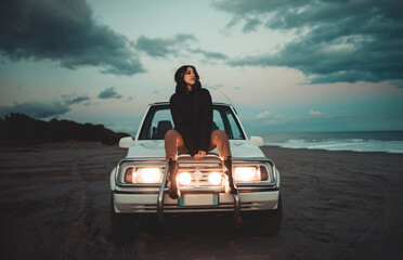 Ragazza seduta in spiaggia con la sua jeep 