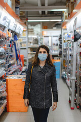 Fototapeta premium Vertical close-up caucasian woman portrait wearing protective face mask walking between shelves store doing shopping. Buy concept.