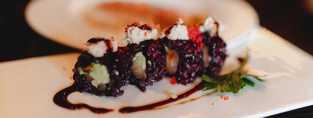 Close-up horizontal banner uramaki sushi salmon roll with black rice and avocado. Japanese Healthy food on decorated plate in restaurant.