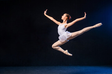 Ballerina in a white dress flying in a jump on black background