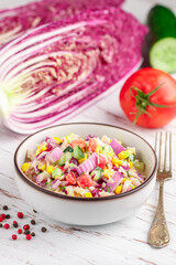 Delicious red Peking cabbage salad with tomatoes, cucumbers, corn, onions and crab sticks in a white plate on a wooden table. Light gourmet dinner. Selective focus